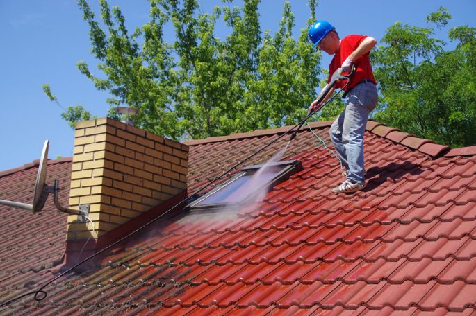 Roof Cleaning A person cleaning a red tiled roof with a pressure washer on a sunny day.