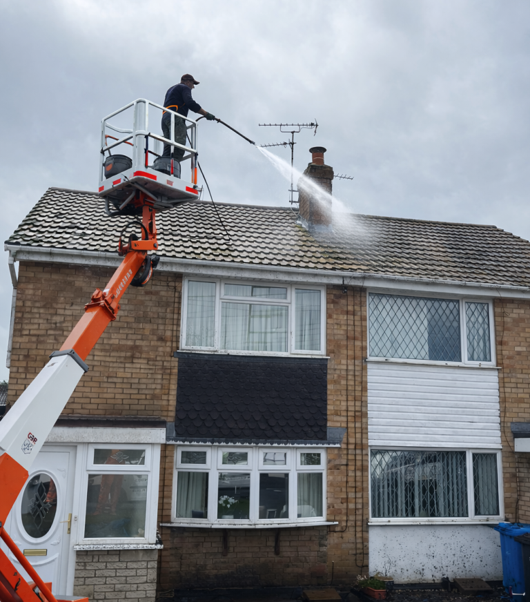 Man cleaning roof in a cherry picker A person on a platform uses a pressure washer to clean a roof.