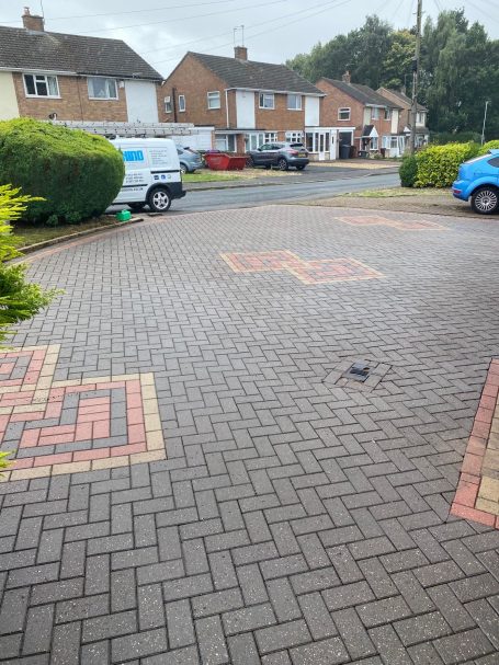 Driveway Cleaning Paved driveway with patterned bricks and residential houses in the background.