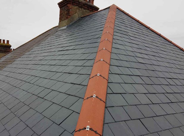 Dry Ridge Slate roof with an orange ridge, showcasing a cloudy sky in the background.