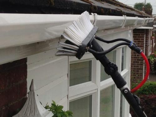 Soffit Cleaning Gutter cleaning tool with bristles and brush, positioned near a house.
