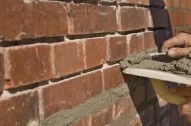Re-Pointing Close-up of a hand applying mortar between red bricks on a wall.